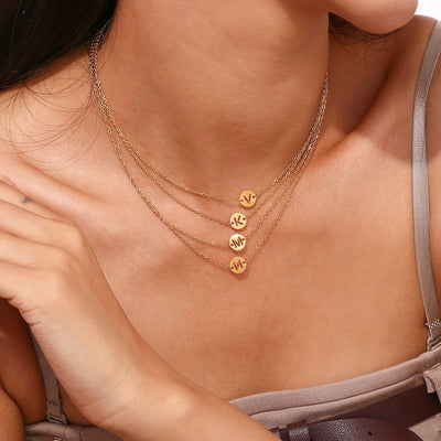 Collar de acero inoxidable dorado o plateado con una medalla pequeña redonda calada en forma de inicial y cadena forzada
