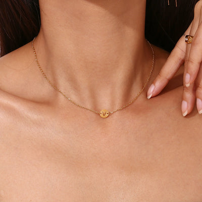 Collar de acero inoxidable dorado o plateado con una medalla pequeña redonda calada en forma de inicial y cadena forzada